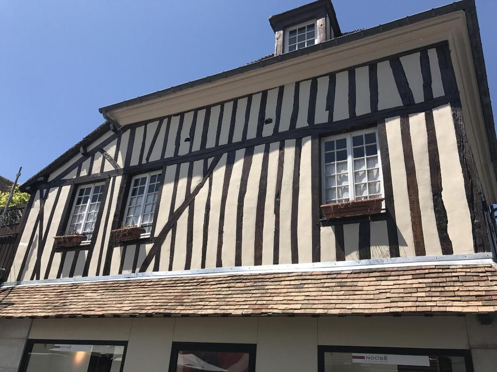 Bâtiment de deux étages avec un toit brun clair et une façade brun foncé et blanche. Fenêtres avec jardinières.
