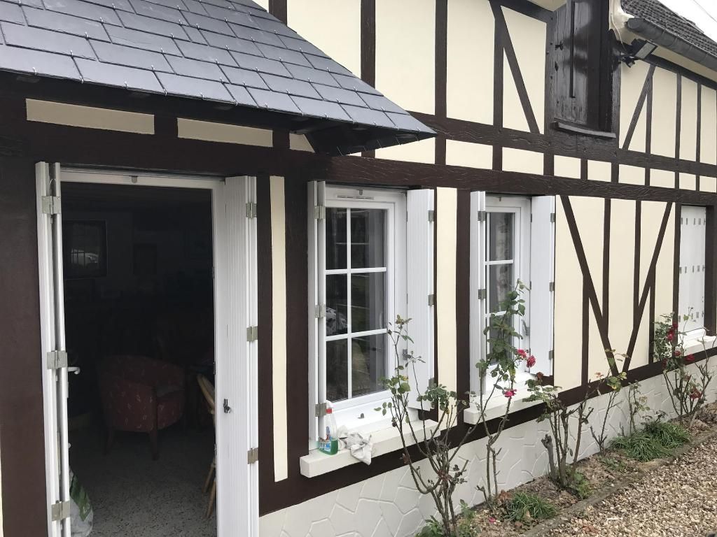 Maison à colombages avec porte ouverte et fenêtres à cadre blanc et volets blancs.