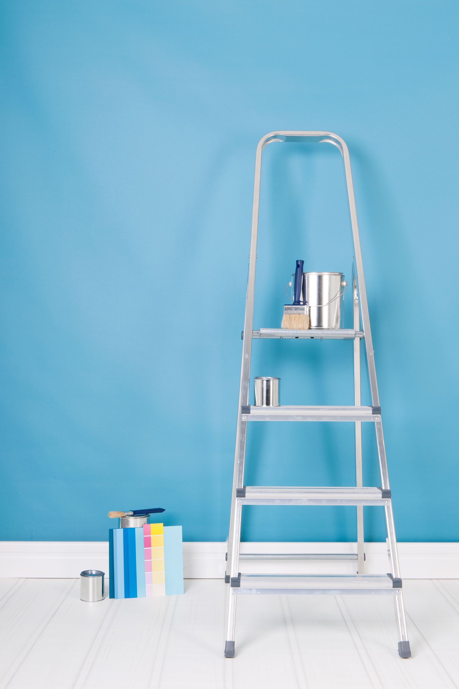Une échelle avec des pots de peinture et du matériel est appuyée contre un mur bleu dans une pièce.