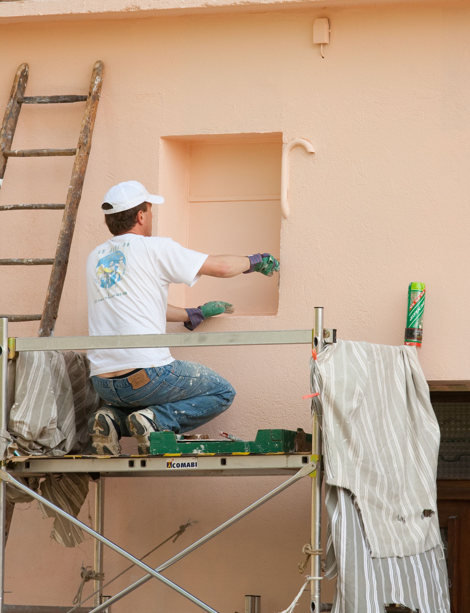 Une personne sur un échafaudage, appliquant du stuc sur un mur, travaillant dans une zone en retrait.