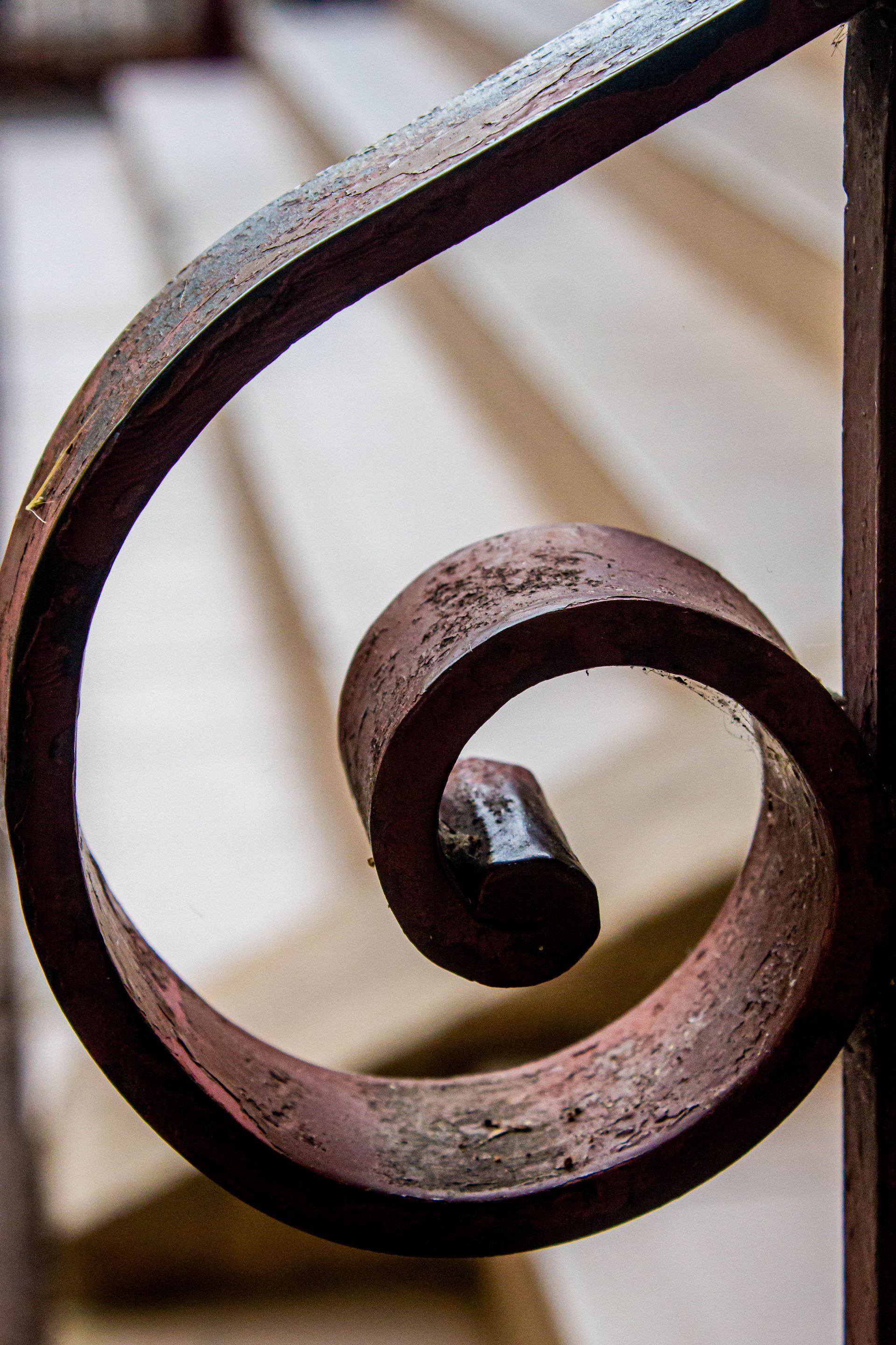 Rambarde en fer rouillé et ornée de volutes ; escalier blanc en arrière-plan.
