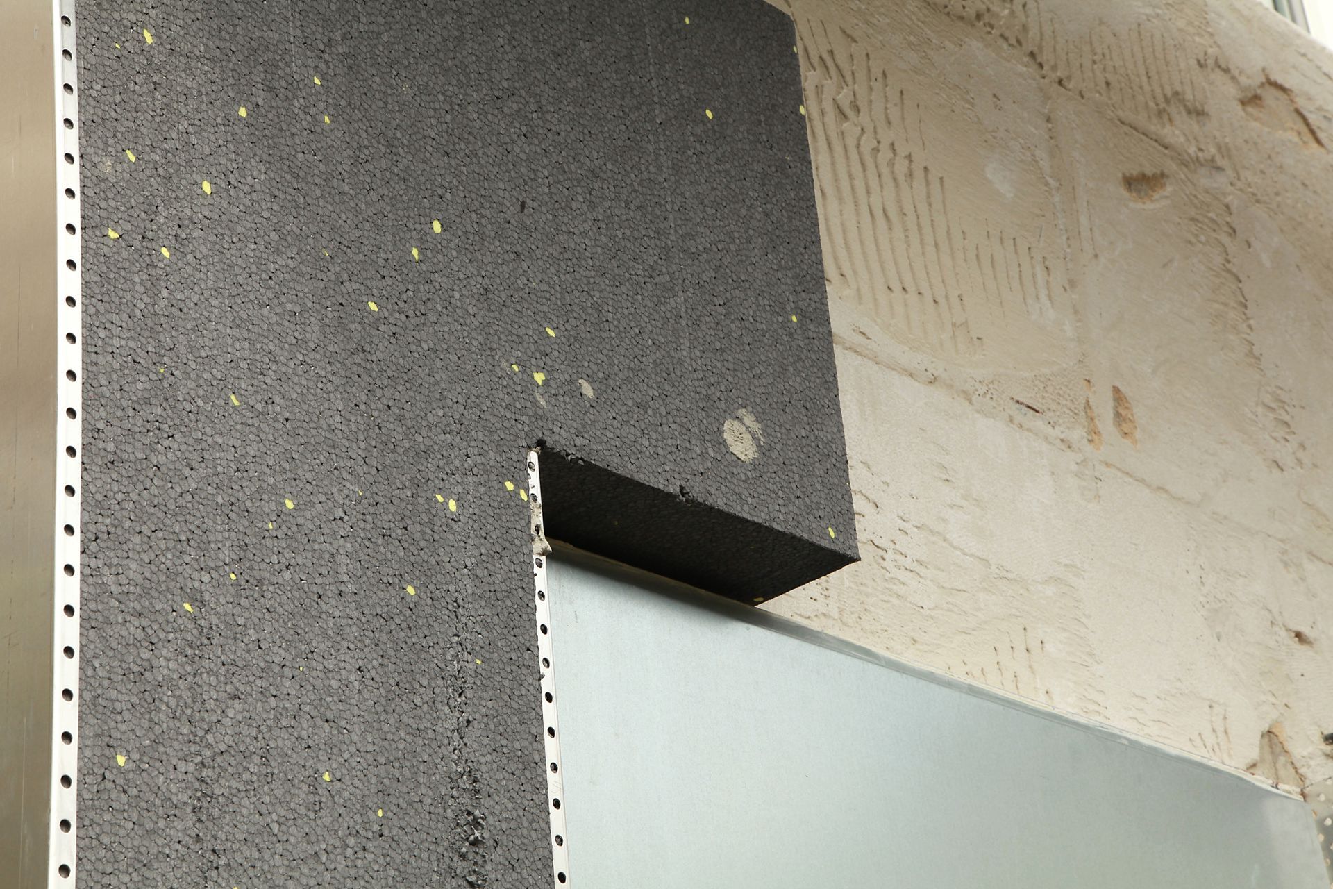 Mur extérieur avec panneau isolant gris autour d'un cadre de fenêtre.