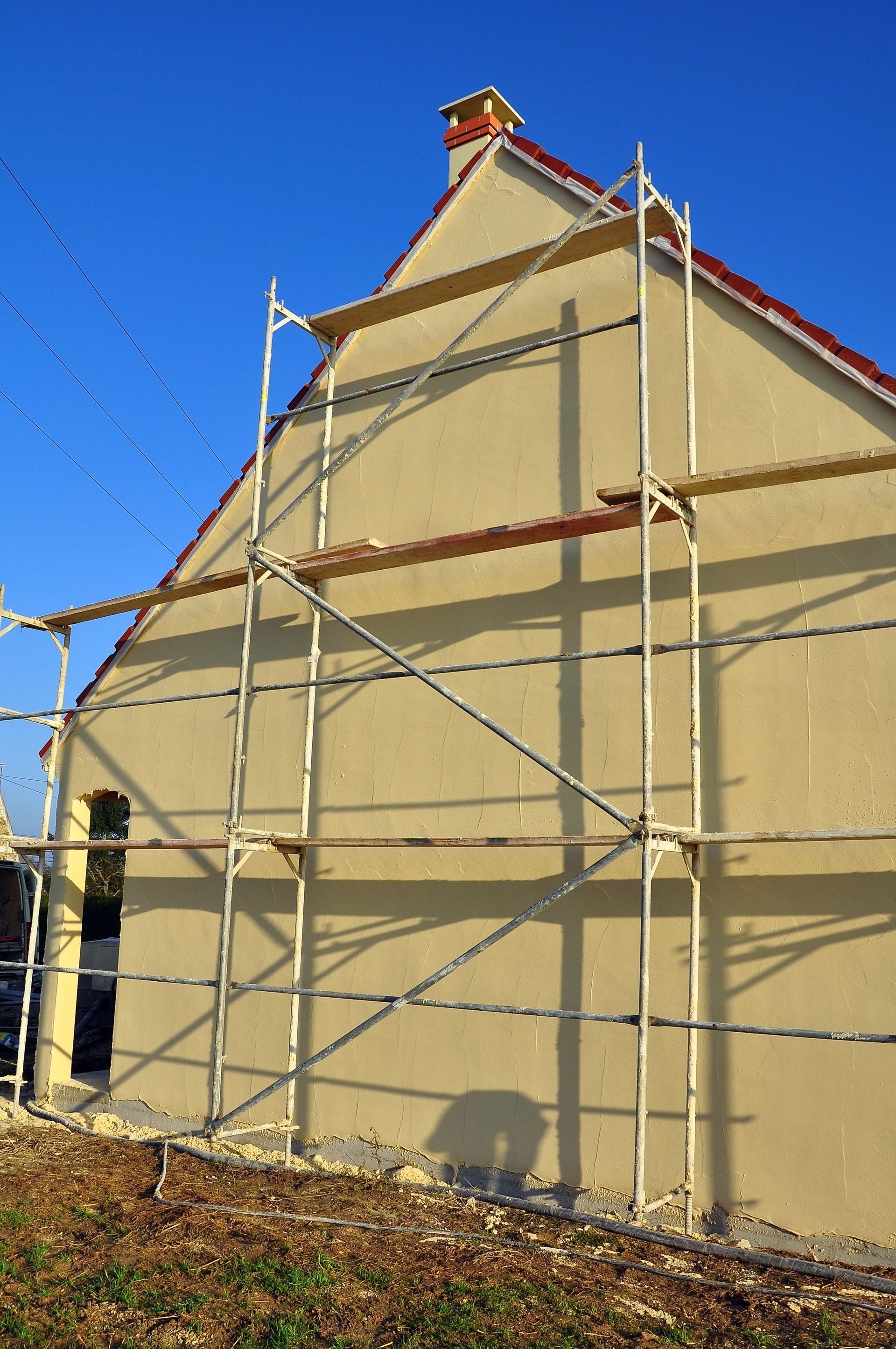 Façade d'une maison en construction, échafaudages contre le mur, ciel bleu.