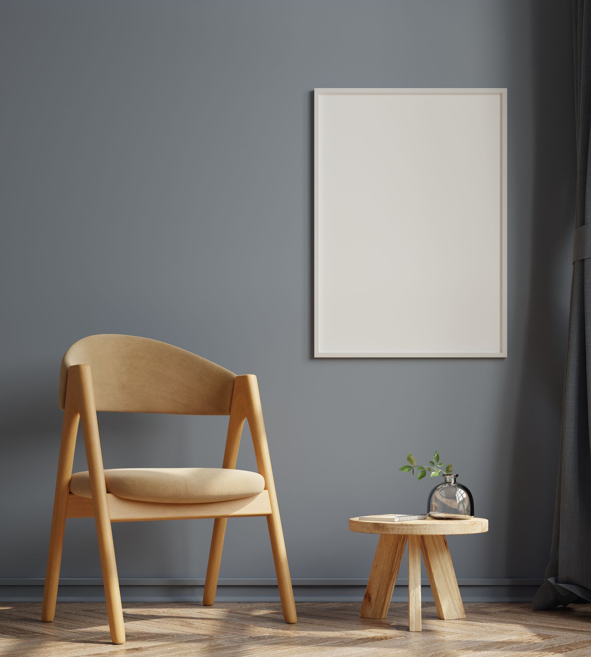 Chaise beige et petite table en bois à côté d'un tableau encadré vierge sur un mur gris.