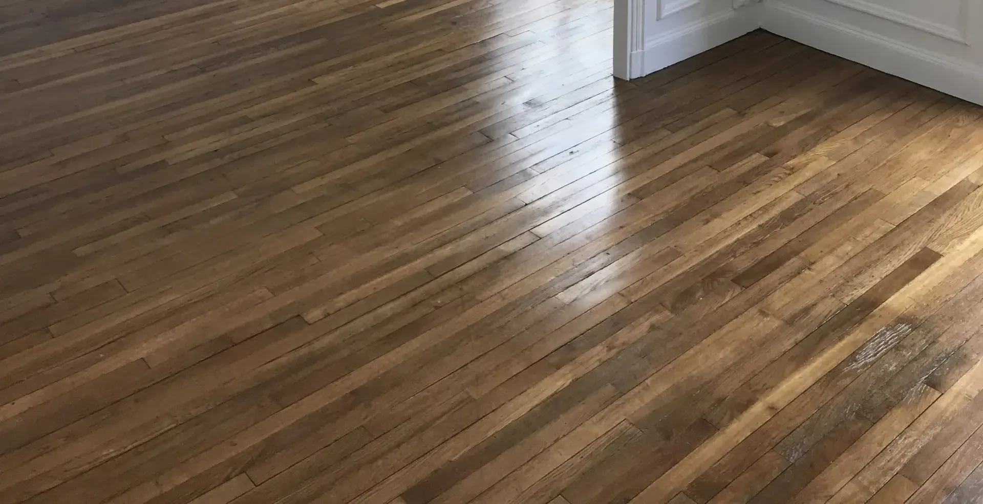 Parquet en bois brillant, reflétant la lumière. Mur blanc adjacent.