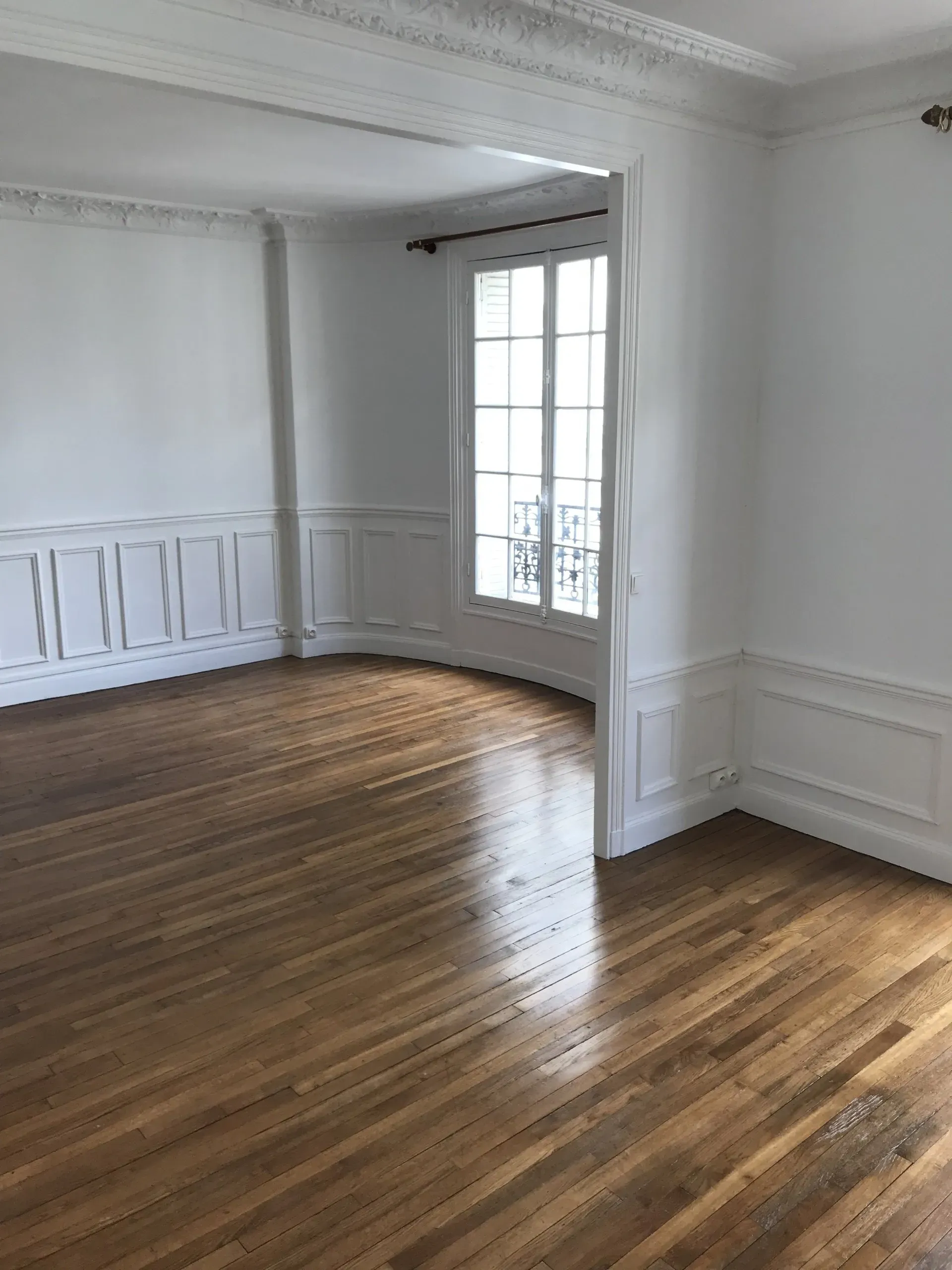 Pièce vide avec parquet, murs blancs, porte et fenêtre.