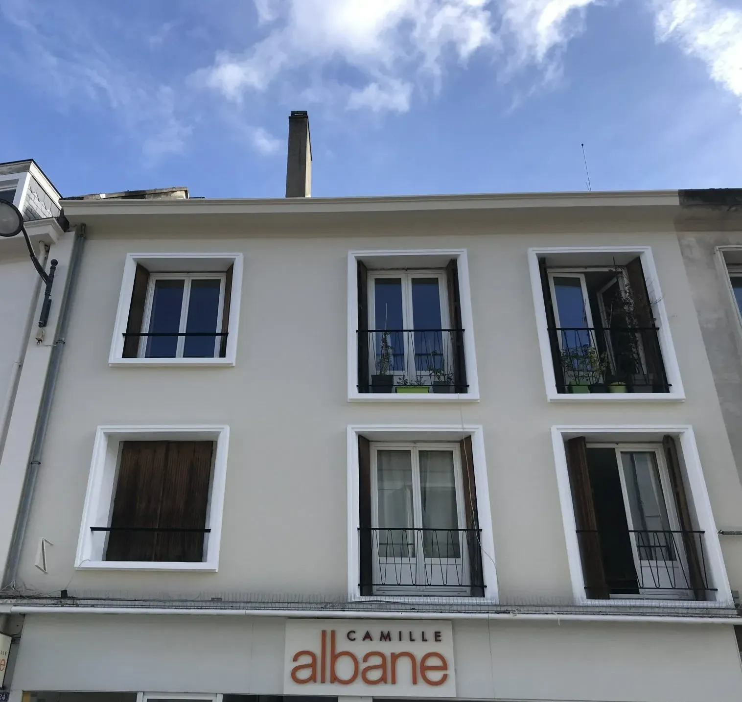 Immeuble de deux étages avec six fenêtres et le nom « Camille Albane » en bas. Ciel bleu.