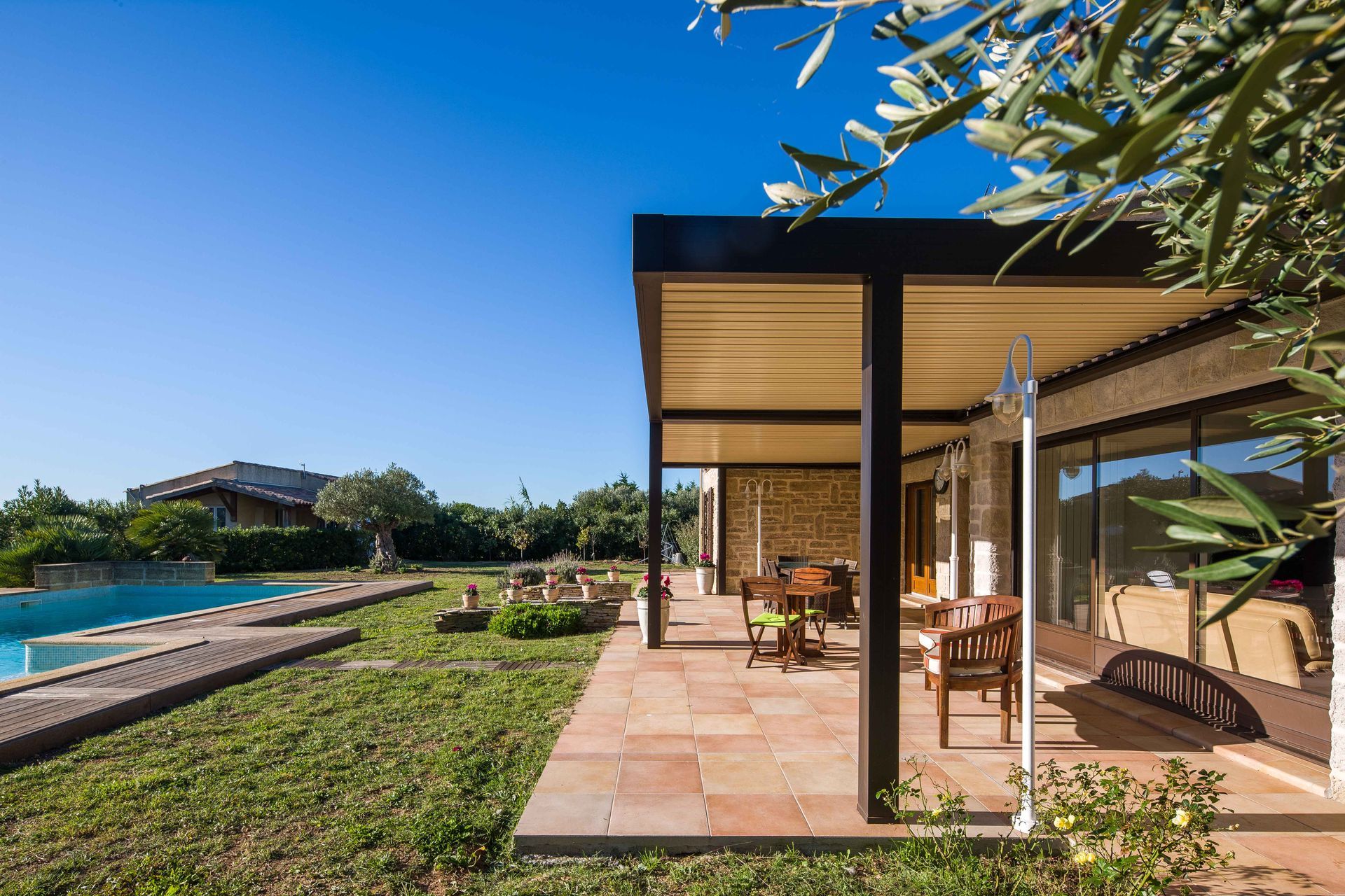 Patio avec table à manger, chaises et auvent donnant sur la piscine par une journée ensoleillée.