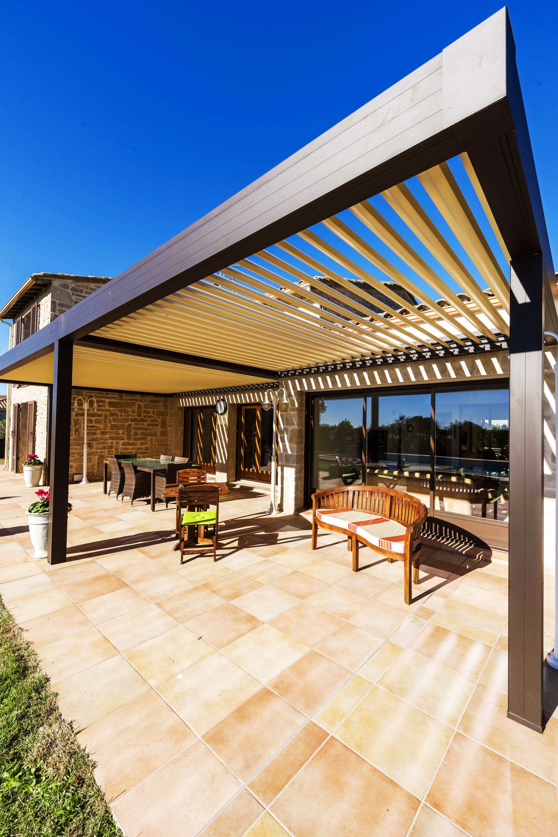 Terrasse extérieure avec pergola, sièges et ciel bleu ensoleillé.