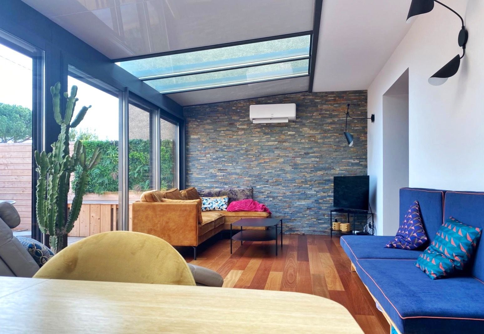 Salon avec parquet, mur en pierre et canapé bleu.