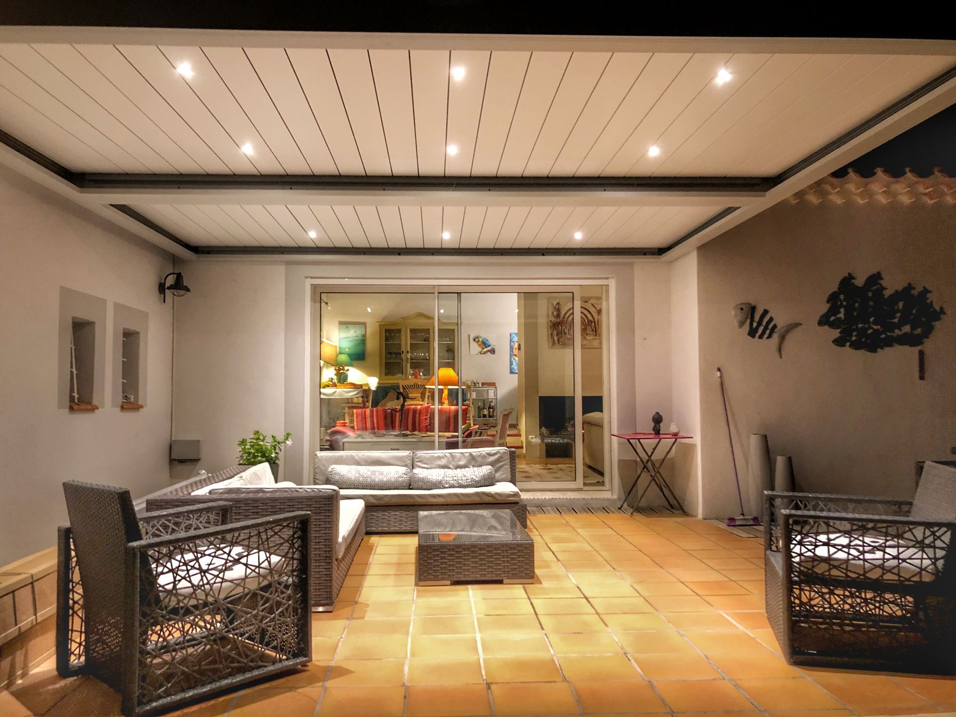 Terrasse extérieure avec mobilier moderne, ouverte sur un espace intérieur éclairé.