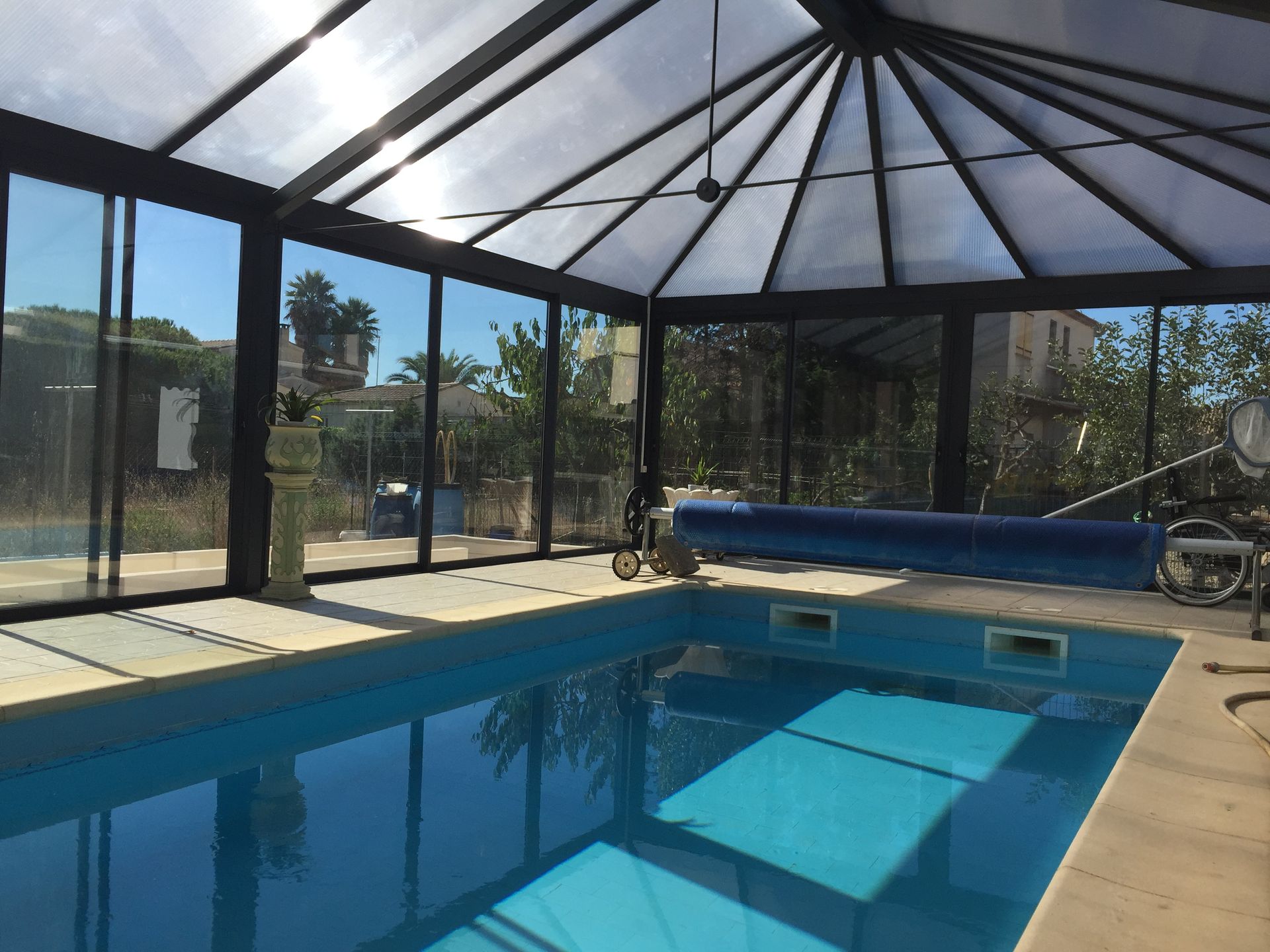 Piscine intérieure avec toit transparent et parois vitrées, eau bleue, lumière éclatante.