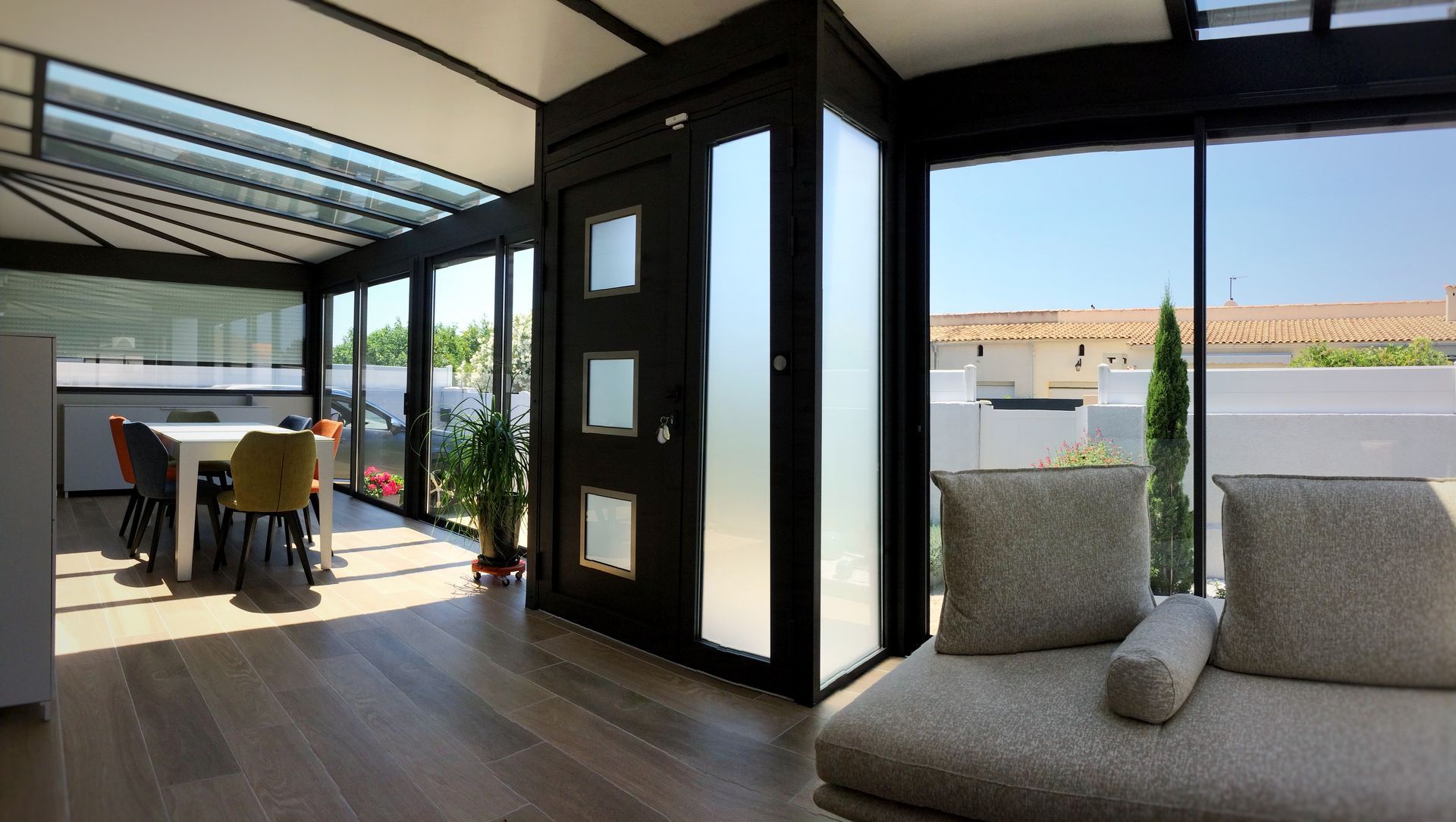 Intérieur de véranda avec un canapé, une table à manger et de grandes fenêtres.