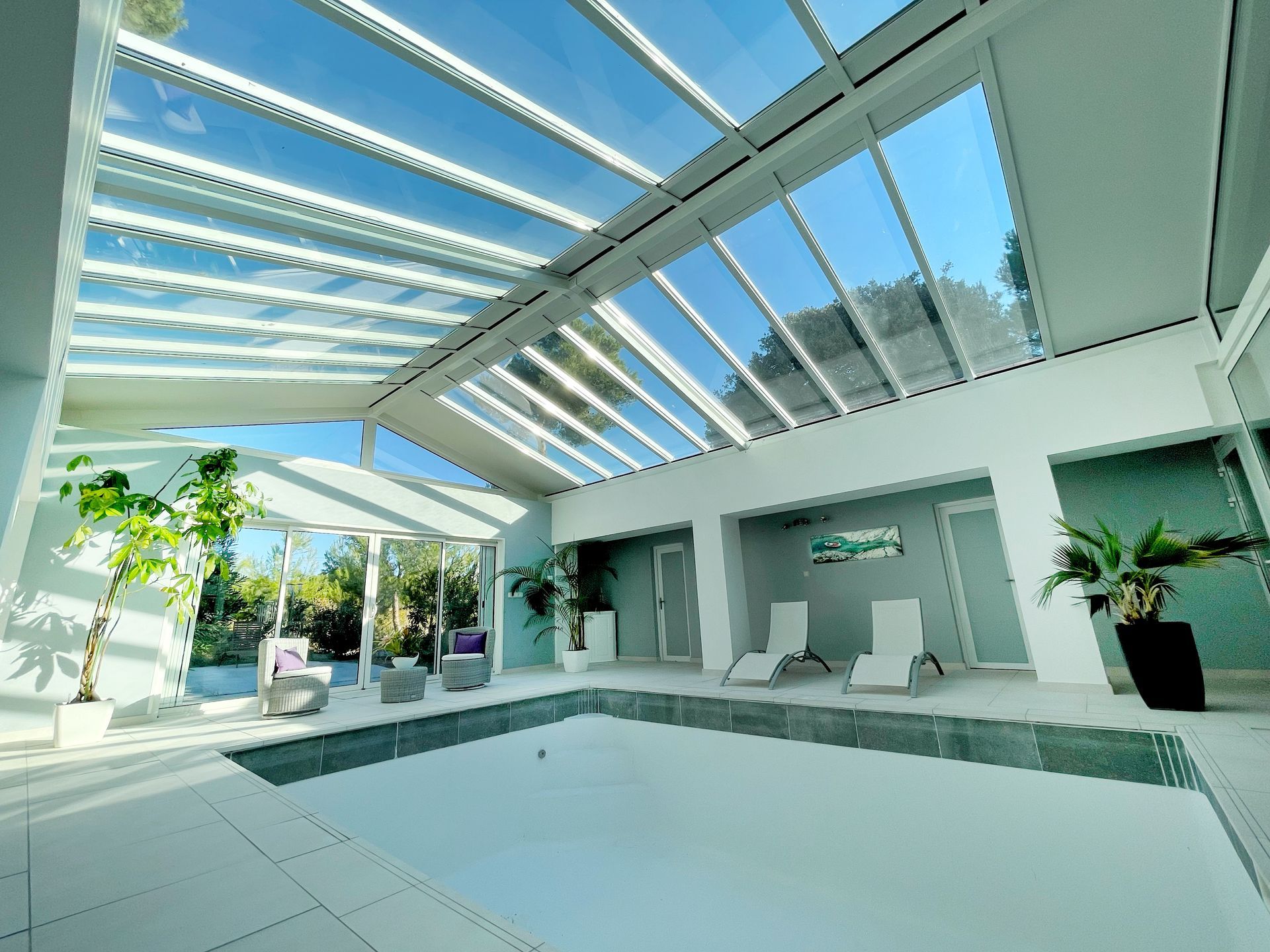 Piscine intérieure avec verrière, transats et plantes, dans une salle lumineuse.