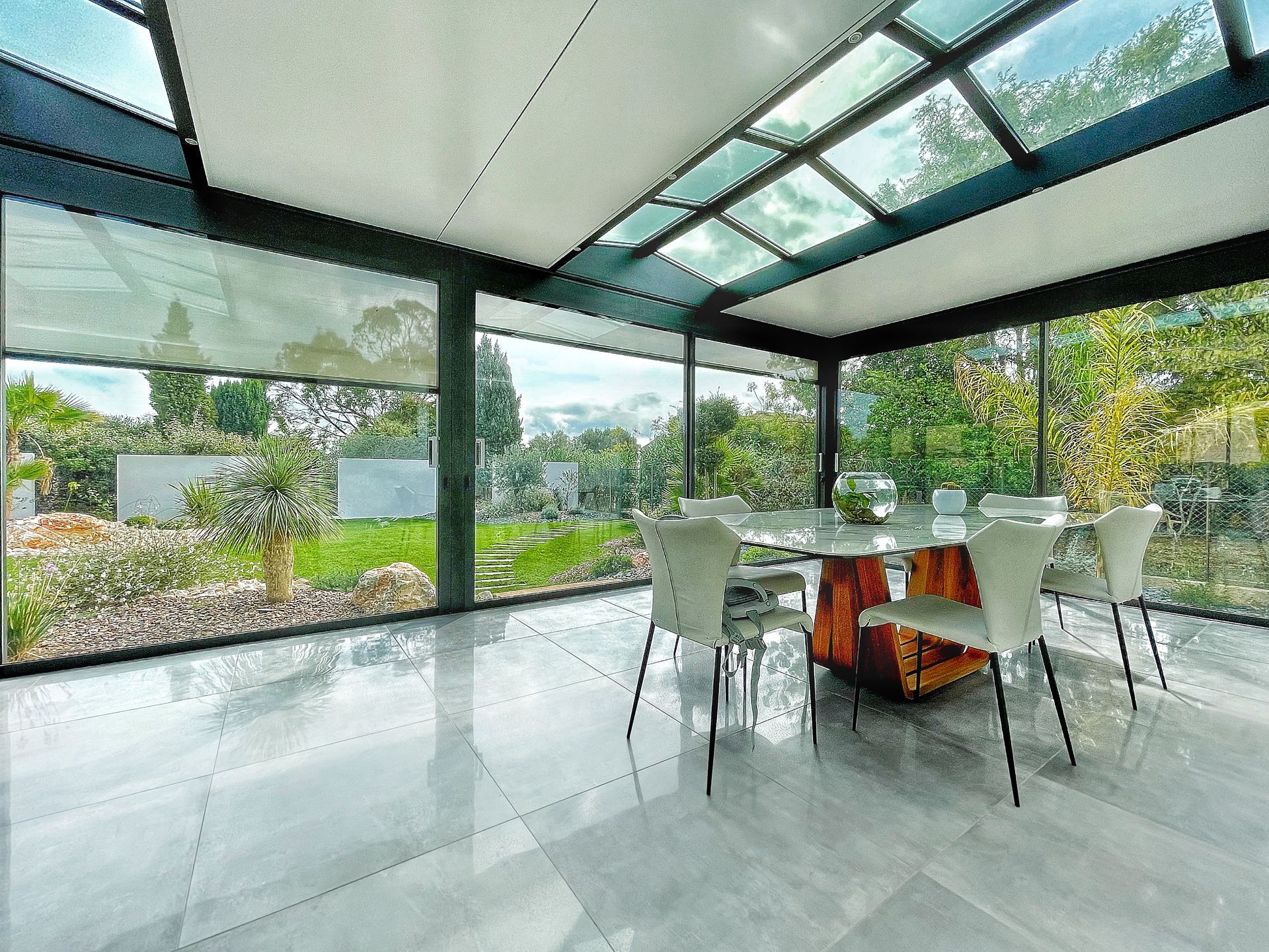 Salle à manger vitrée avec table, chaises et vue sur le jardin. La lumière naturelle inonde l'espace.
