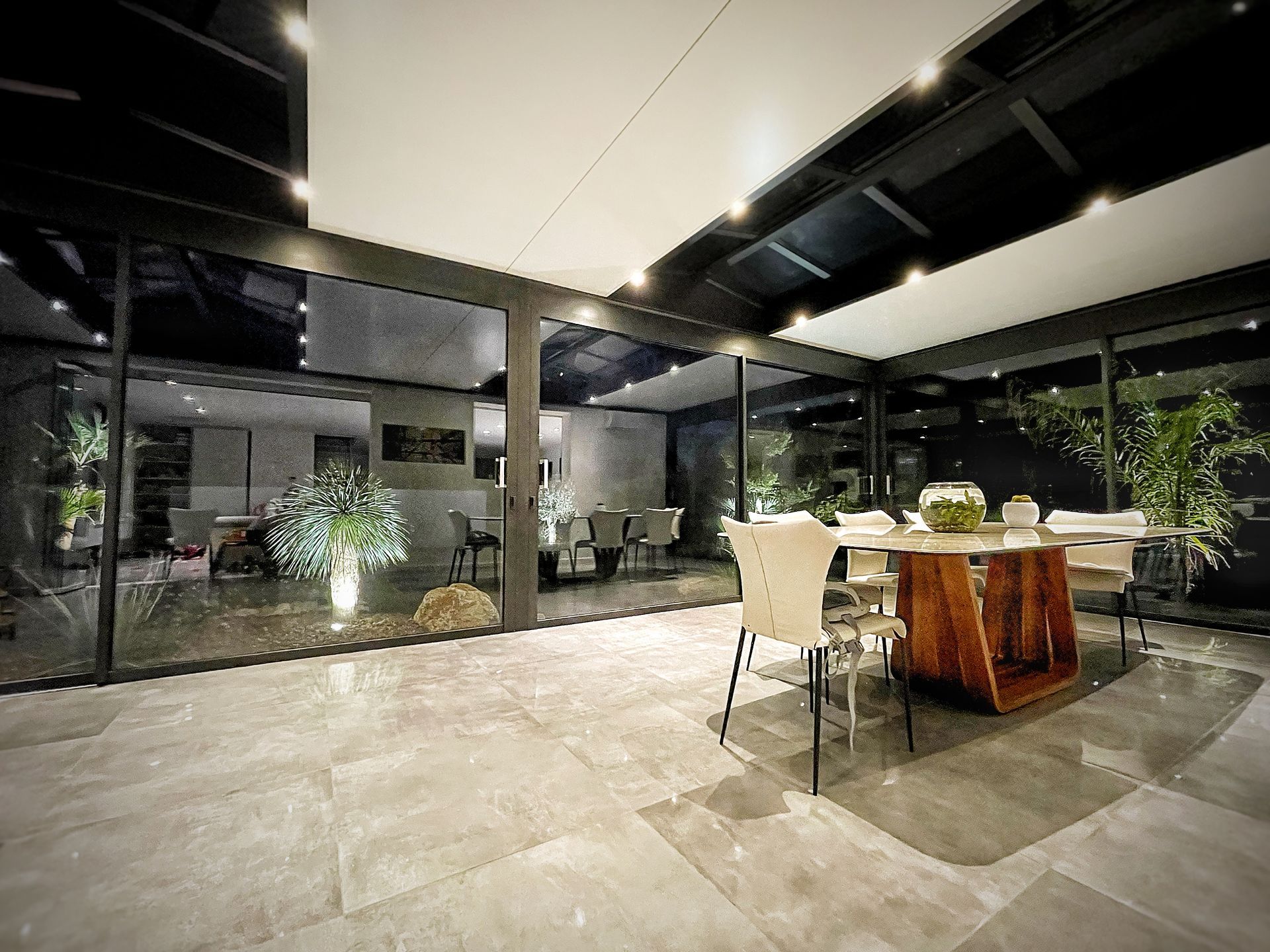 Salle à manger avec murs en verre, mobilier moderne et sol en carrelage gris.