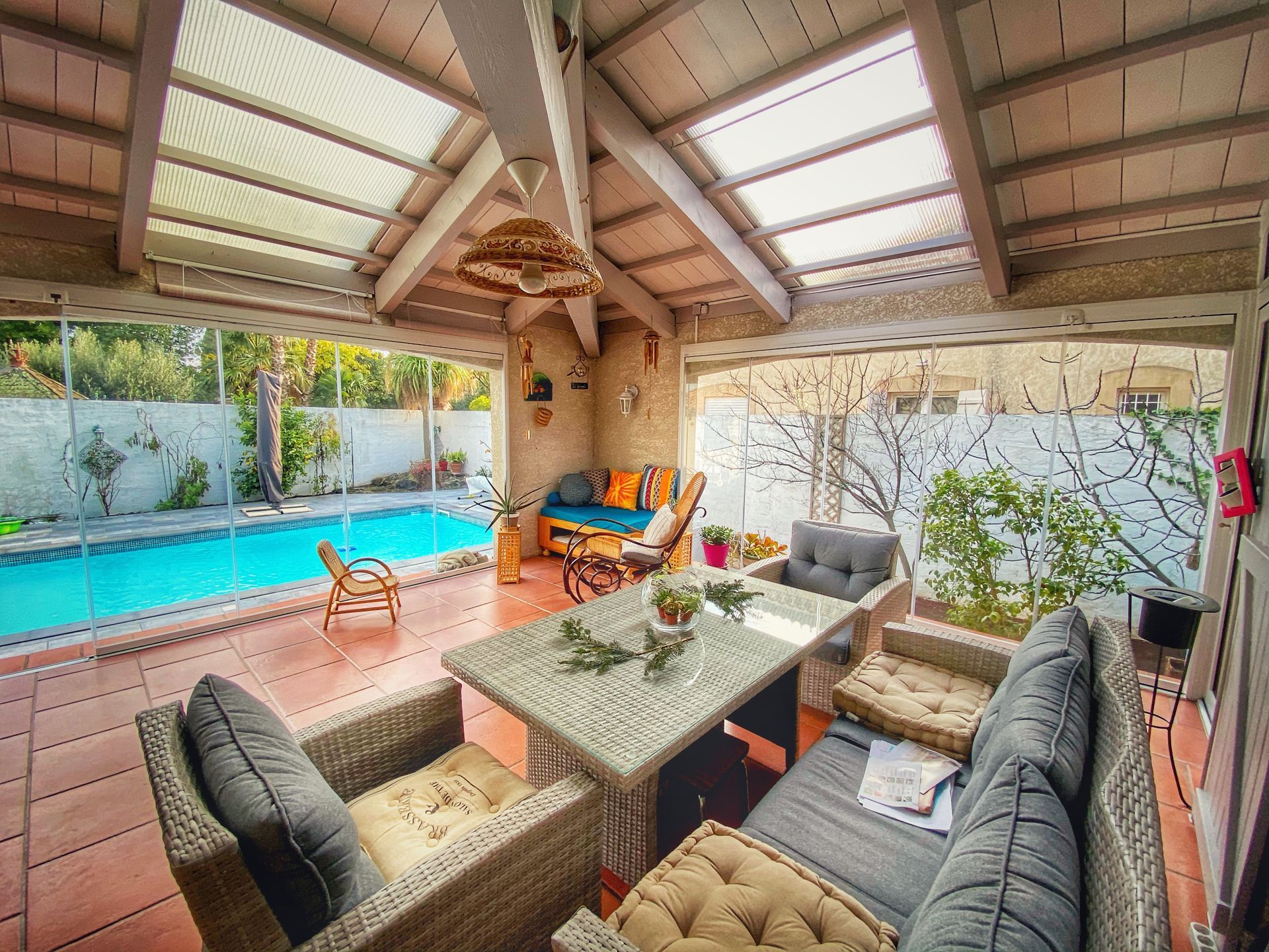 Un patio couvert avec vue sur la piscine comprenant des meubles en osier et une table à manger.
