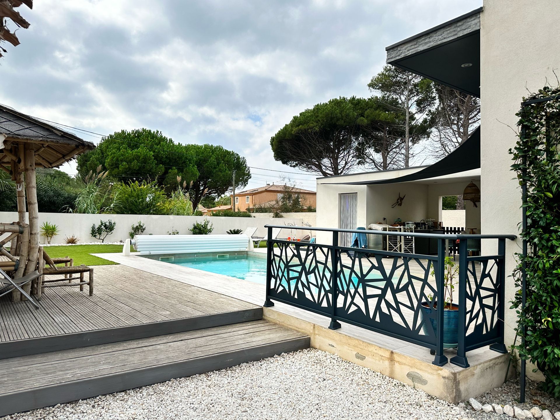 Piscine arrière avec balustrade noire décorative, marches et arbres par temps nuageux.