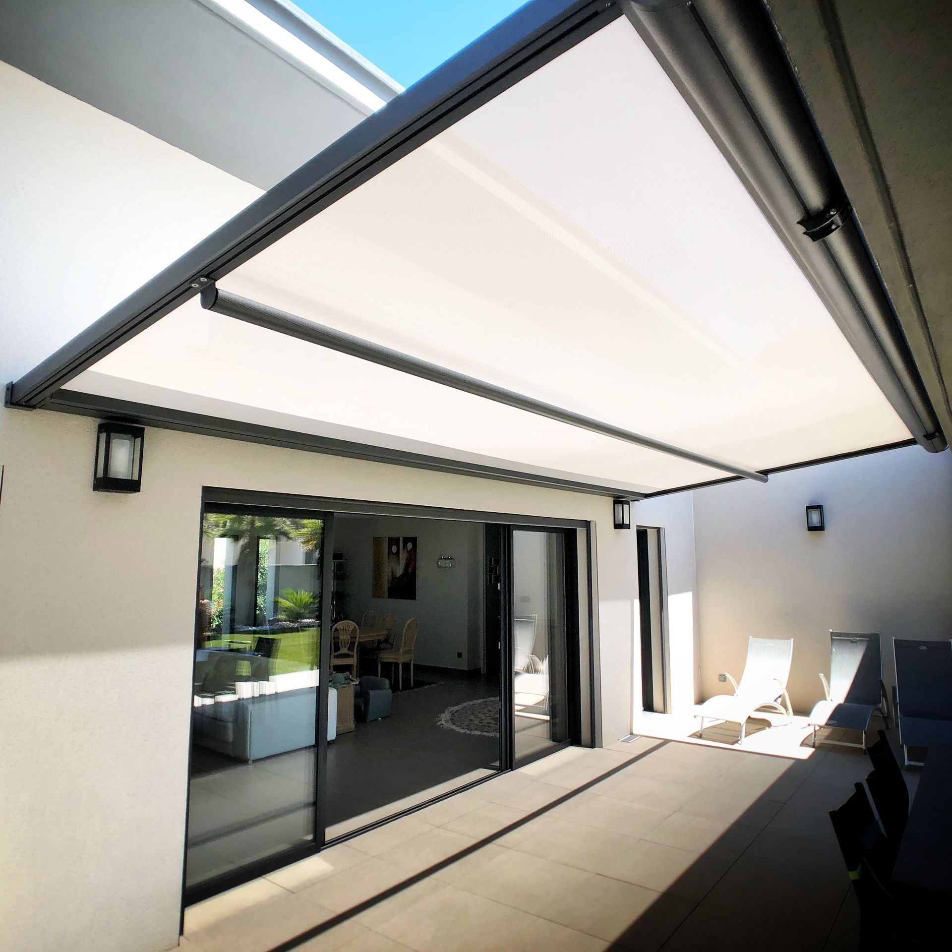 Auvent rétractable blanc ombrageant un patio avec portes coulissantes et quelques chaises.