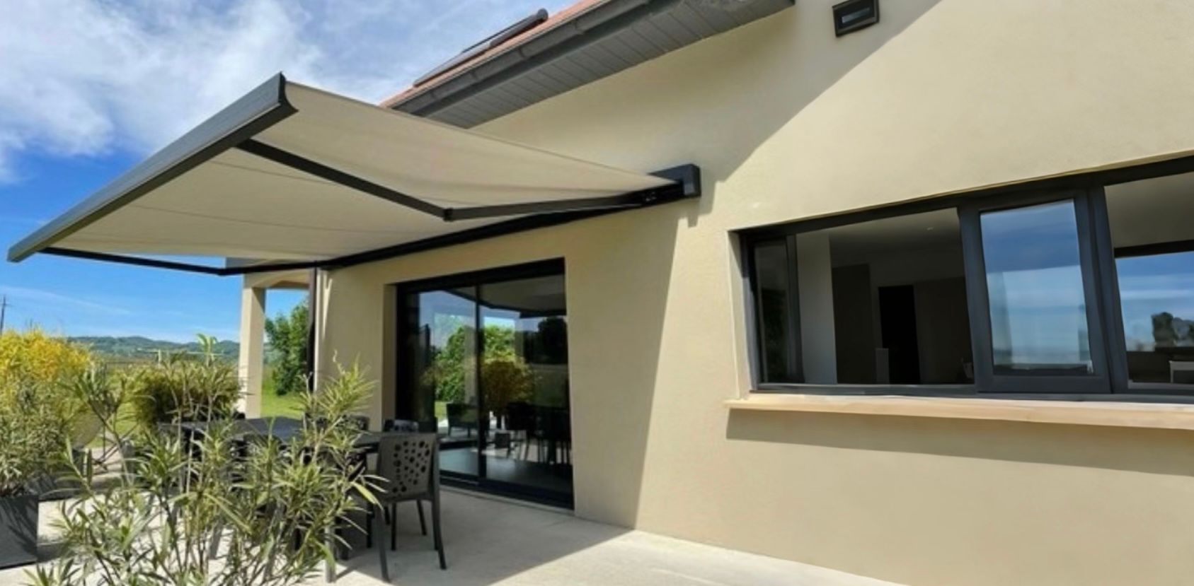 Terrasse d'une maison avec auvent, et porte-fenêtre coulissante. Les murs du bâtiment sont beiges, sur fond de ciel bleu.