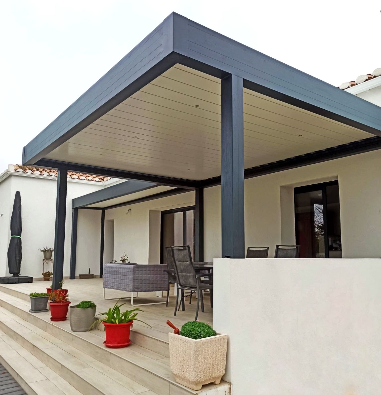 Terrasse couverte avec charpente gris foncé, plafond beige et marches y menant.