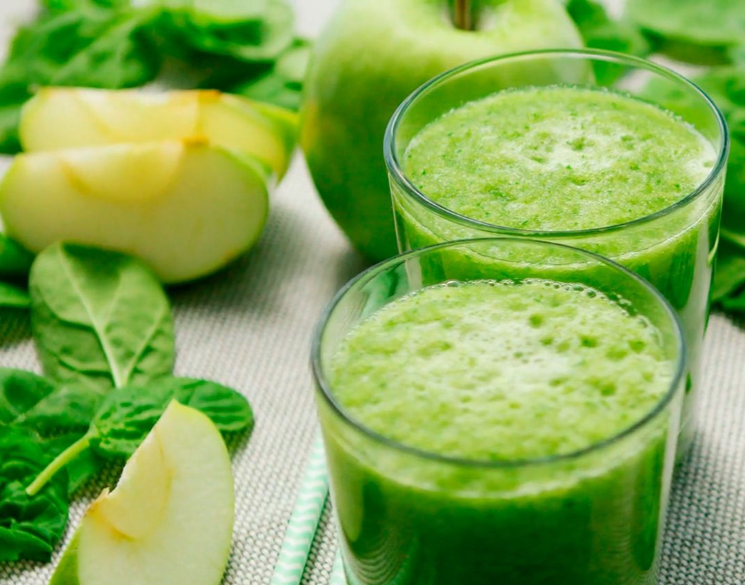Zwei Gläser grüner Smoothie mit Spinat, grünen Äpfeln und Blattgemüse auf einem hellen Tuch.