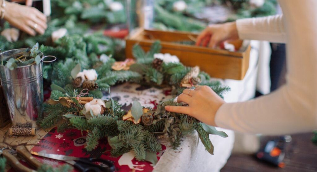 Hands creating festive holiday wreaths with evergreen branches and pinecones at Cannon Beach Christmas workshop near Gearhart Oregon vacation rentals