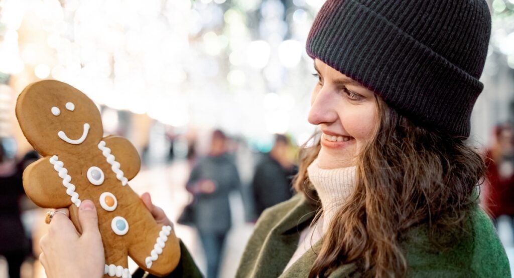 Smiling woman holding gingerbread man cookie at Seaside Oregon Christmas artisan market near Gearhart, Northern Oregon Coast holiday shopping tradition