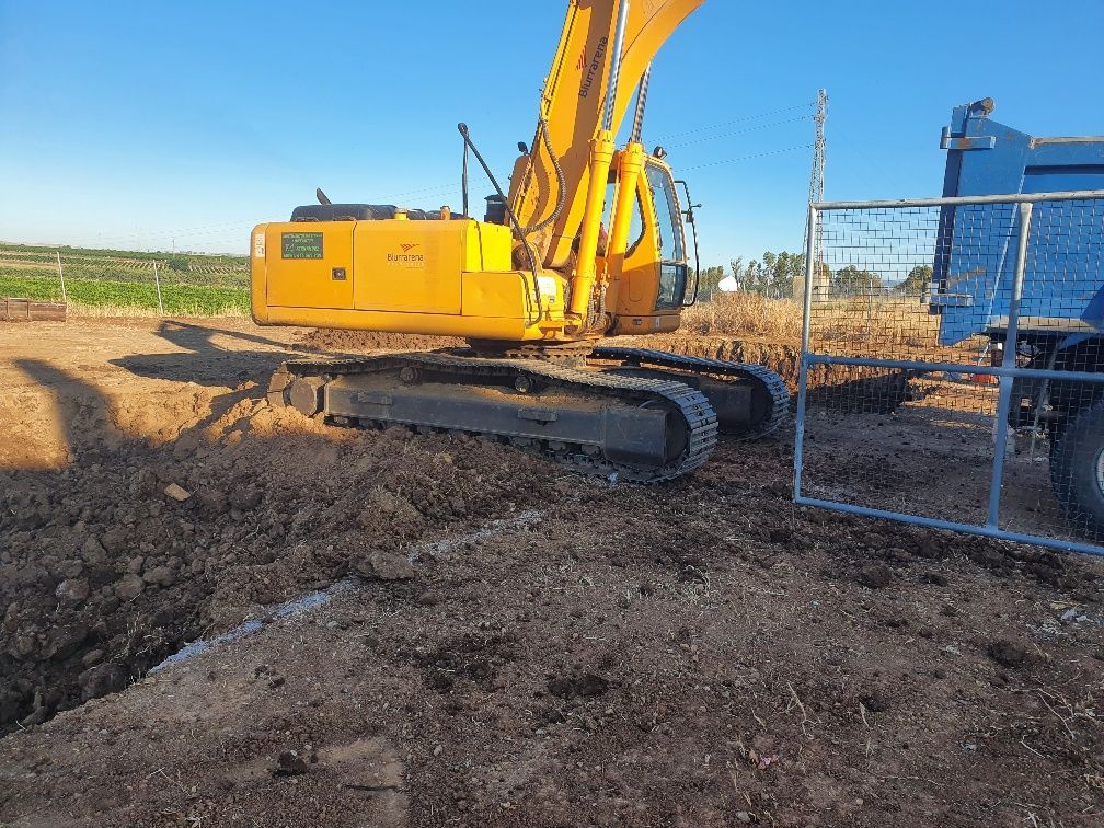 Una excavadora amarilla está sentada en la tierra al lado de un camión volquete azul.