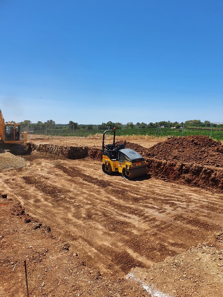 Una excavadora y un rodillo están trabajando en un campo de tierra.