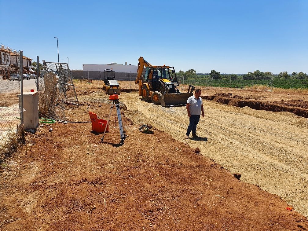 Un hombre está parado en un camino de tierra al lado de una excavadora.