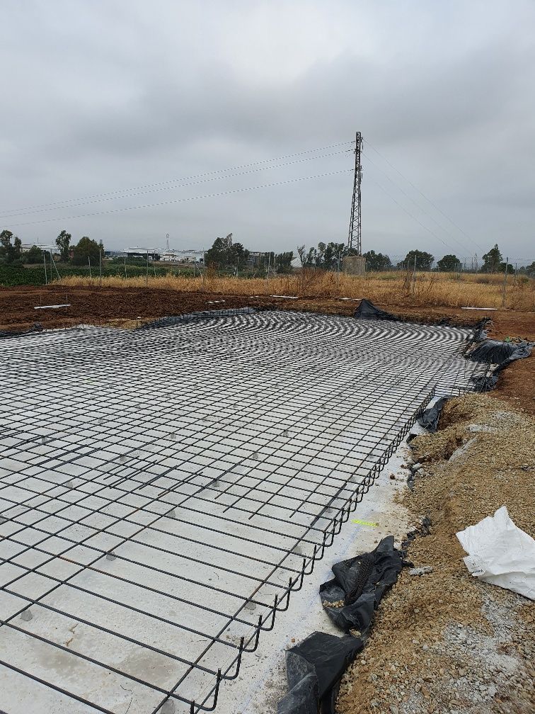 Se está construyendo una base de hormigón en un campo con un poste telefónico al fondo.