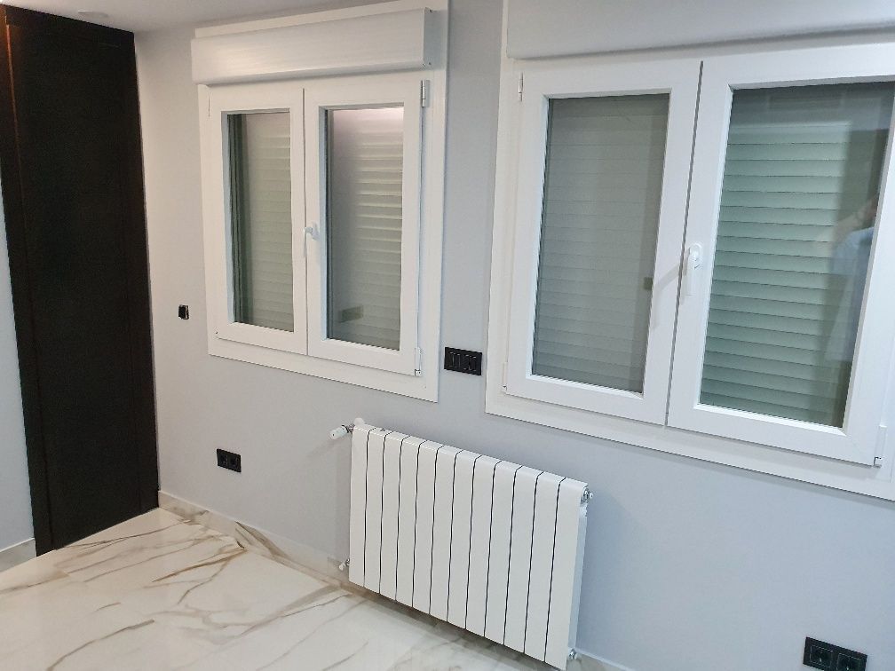 Una habitación con dos ventanas y un radiador en el suelo.