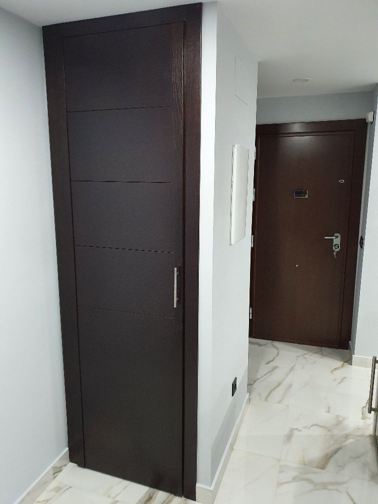 Un pasillo con una puerta marrón y una pared blanca.