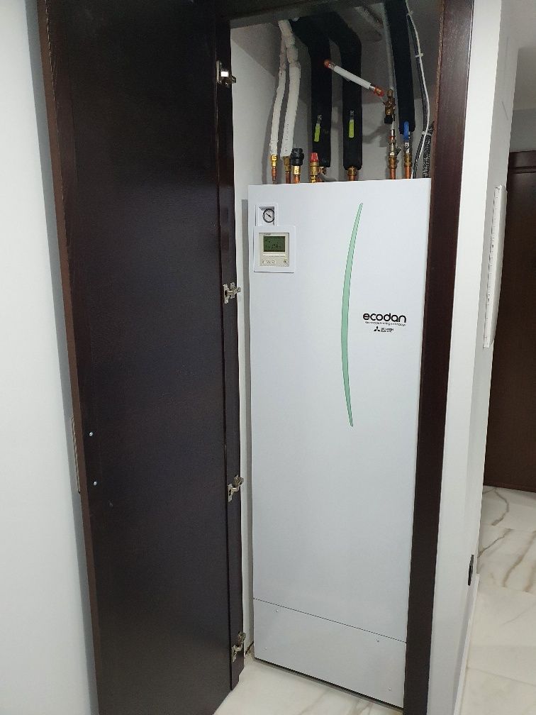 Un refrigerador blanco está sentado en un armario al lado de una puerta.