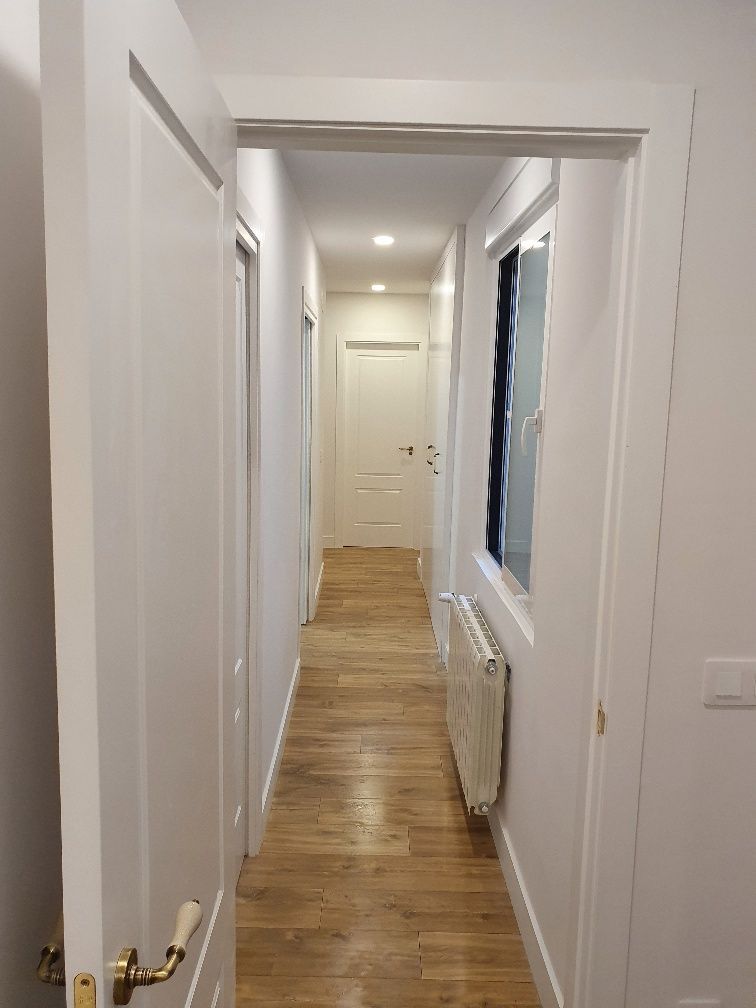 Un largo pasillo con pisos de madera y puertas blancas que conducen a una ventana.