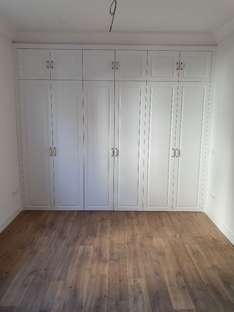 Una habitación vacía con armarios blancos y suelos de madera.