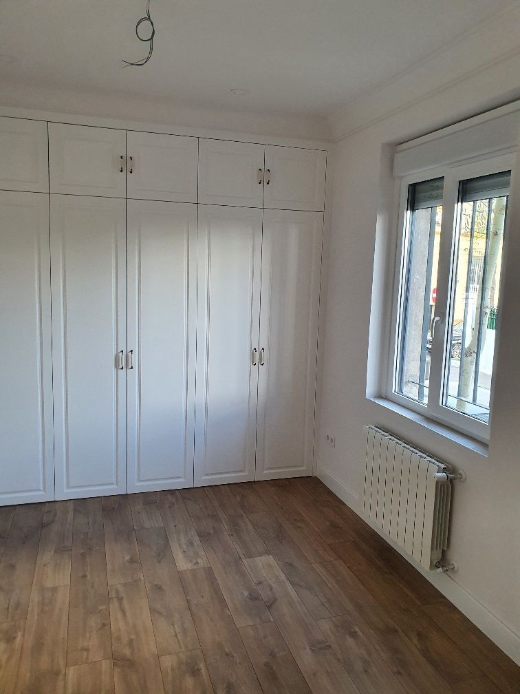 Una habitación vacía con armarios blancos y un radiador.