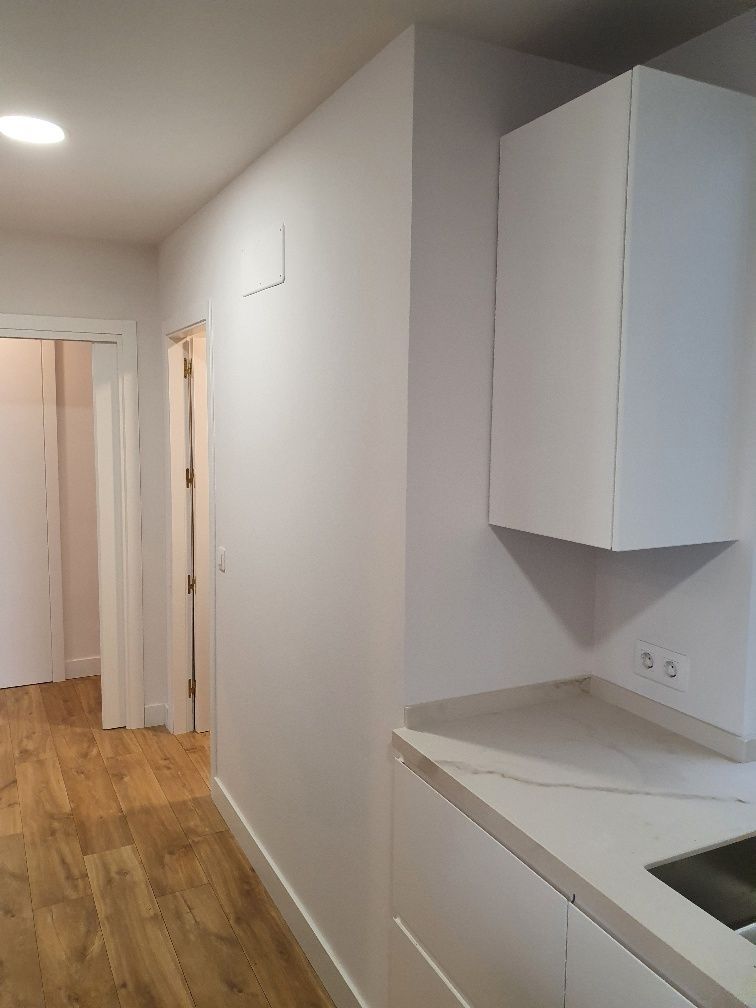 Una cocina con gabinetes blancos y un fregadero en un pasillo.