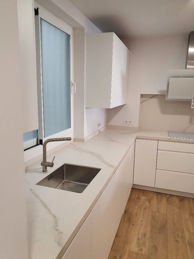 Una cocina con gabinetes blancos y un fregadero y una ventana.