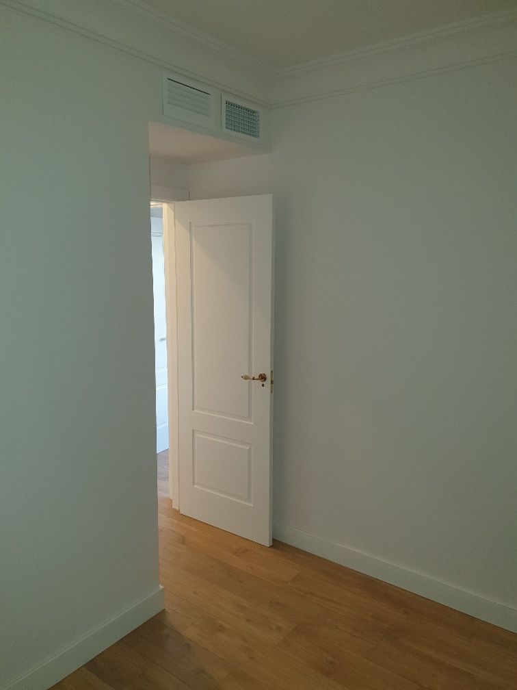 Una habitación vacía con una puerta blanca y suelo de madera.