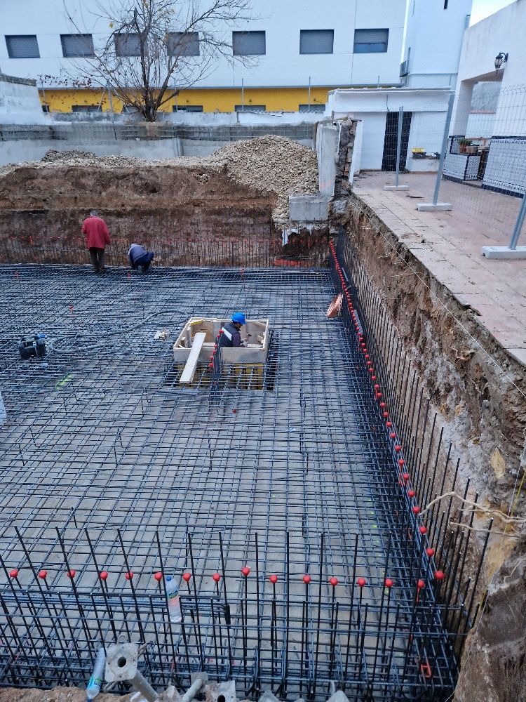 Un sitio de construcción con un gran agujero en el suelo y un edificio al fondo.
