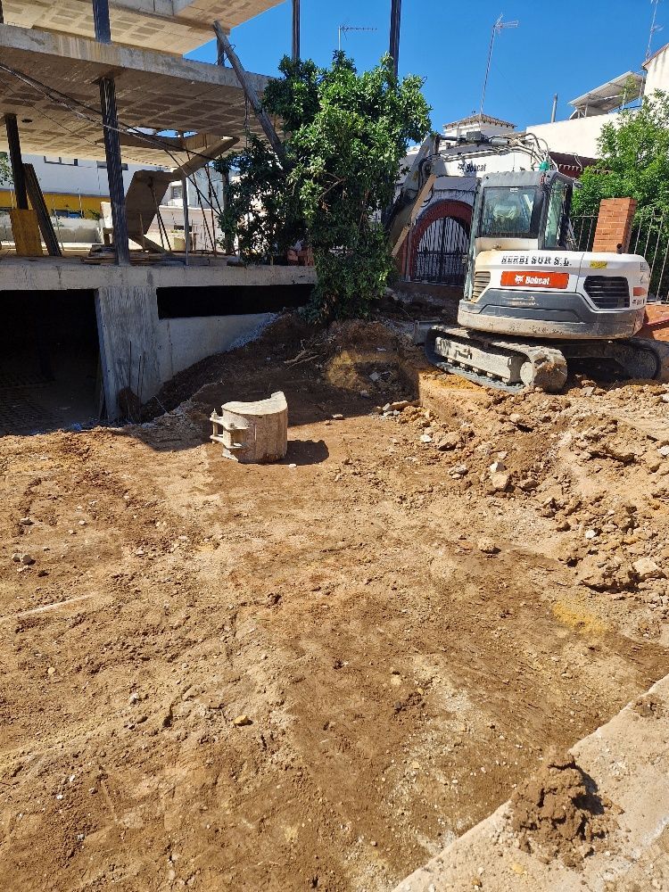 Una excavadora está cavando un hoyo en la tierra frente a un edificio en construcción.