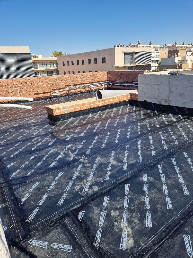 Se está impermeabilizando el techo de un edificio con una membrana negra.