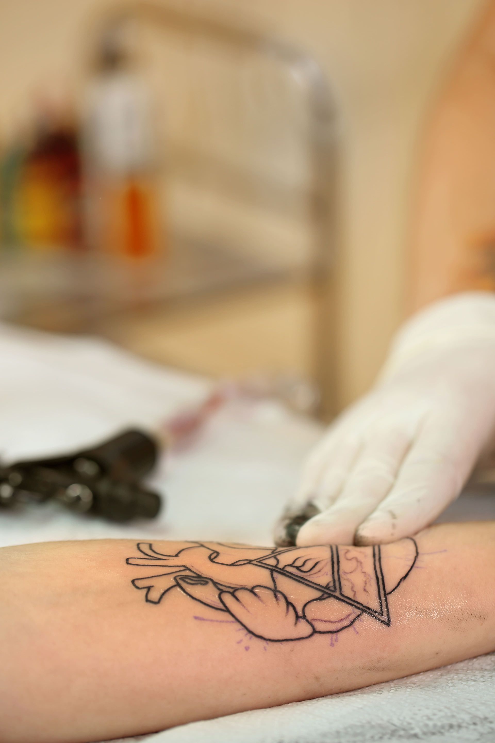 Un tatuador con guantes está tatuando un diseño de un corazón y formas geométricas en el brazo de una persona.