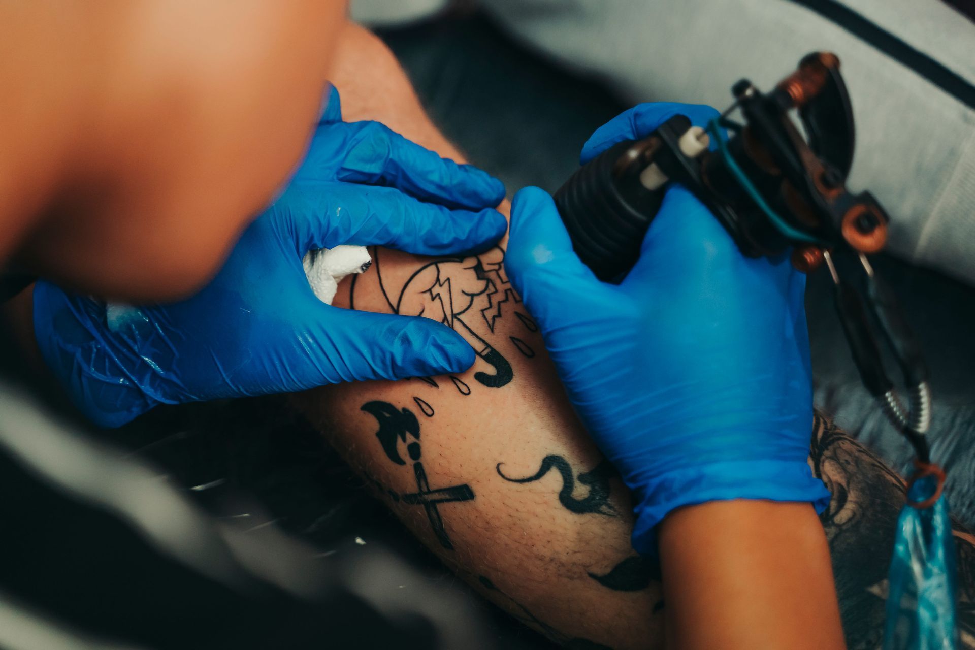 Brazo de una persona siendo tatuado con un diseño negro. El tatuador lleva guantes azules.