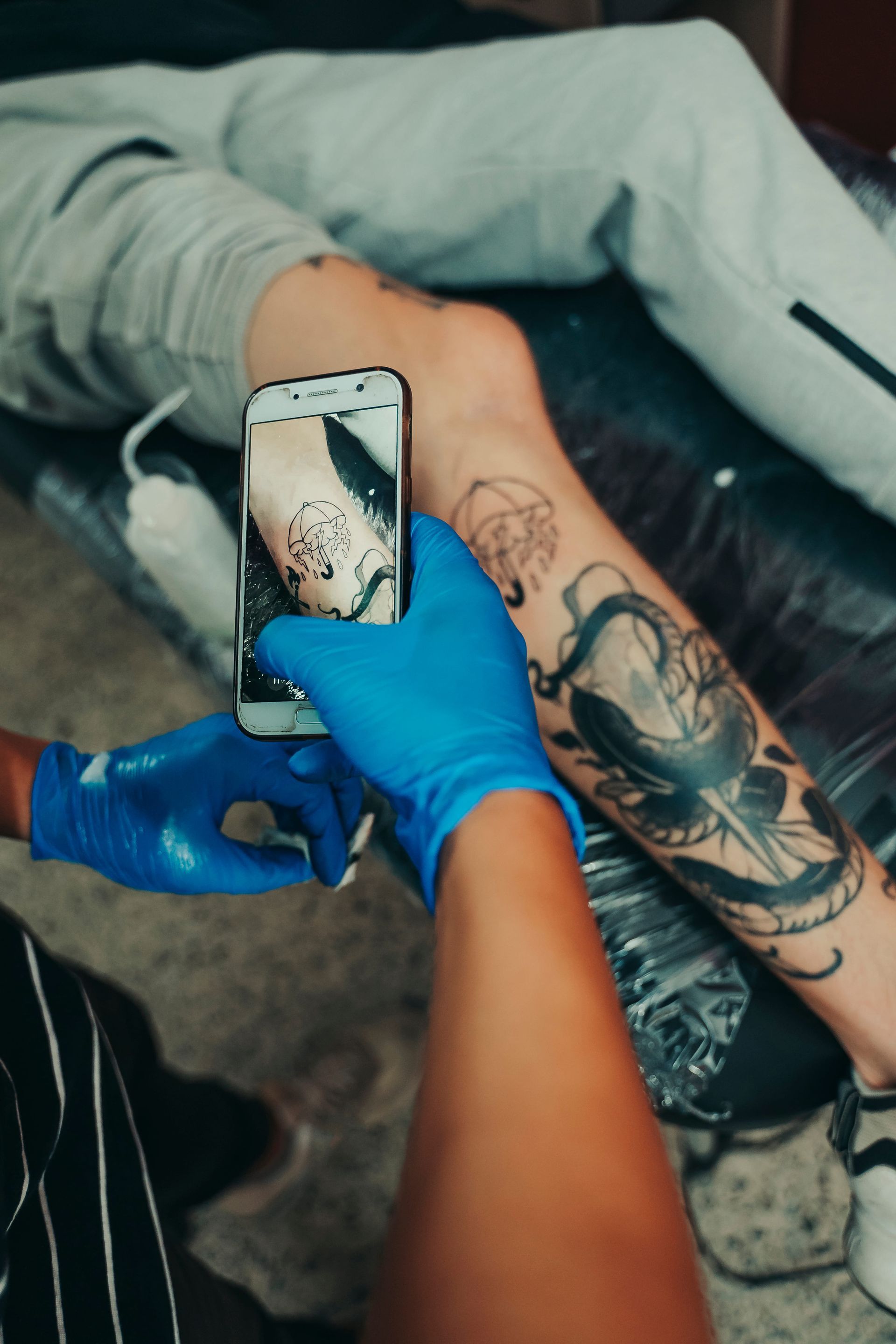 Persona tomando una foto de un tatuaje en la pierna con un teléfono inteligente, en un estudio de tatuajes.