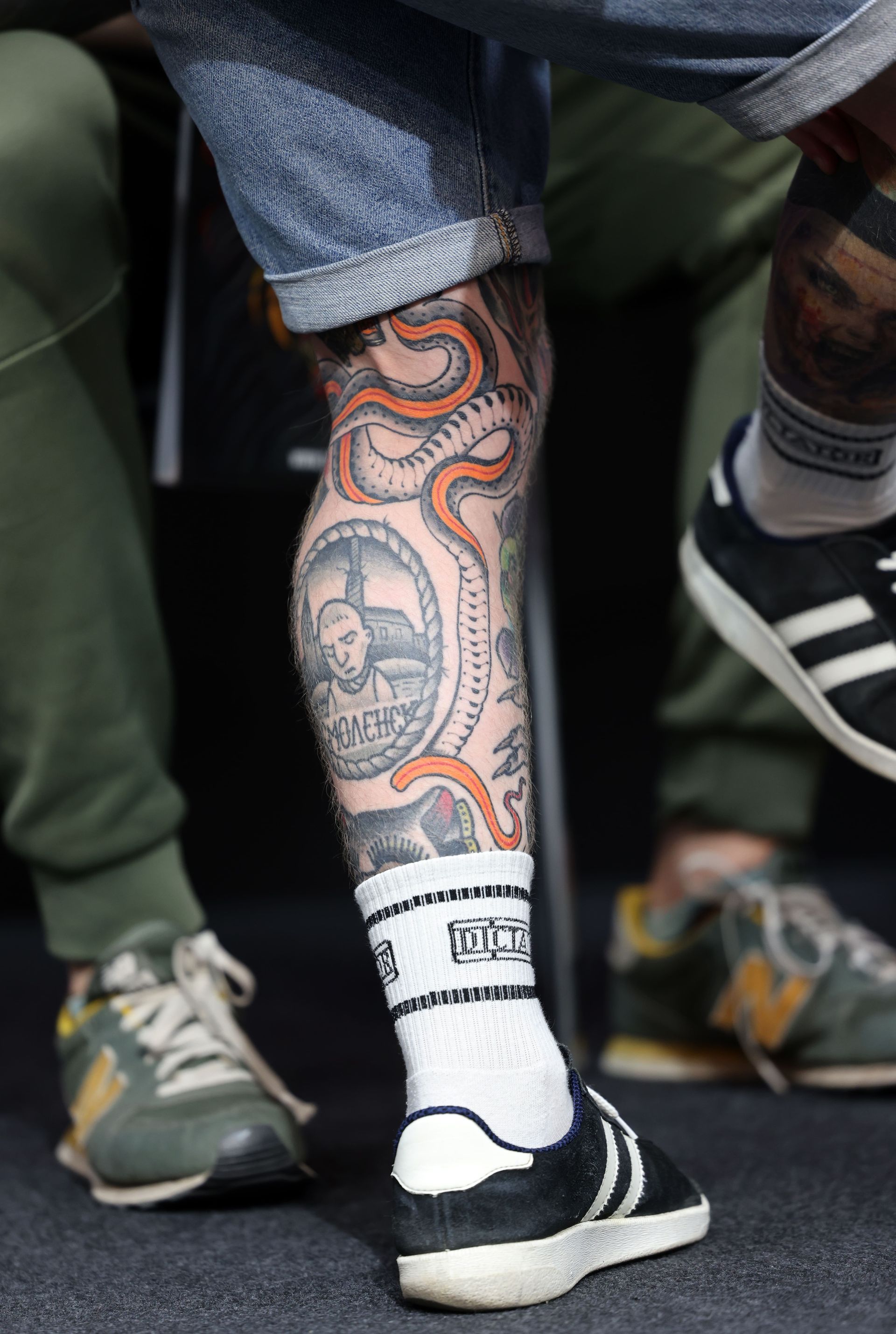 Pierna con tatuajes, pantalones cortos vaqueros, calcetines blancos y zapatillas negras.