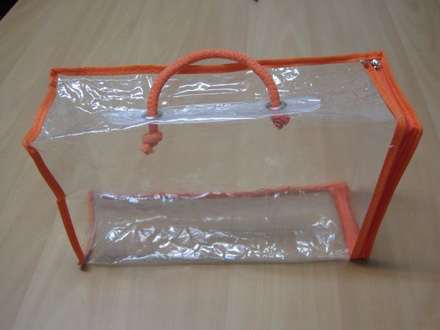 Una bolsa de plástico transparente con asas naranjas sobre una mesa de madera.
