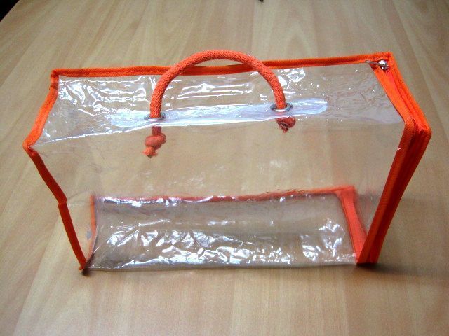 Una bolsa de plástico transparente con asas naranjas reposa sobre una mesa de madera.